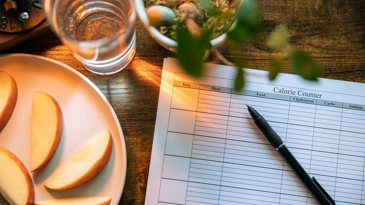 Apple slices, water glass, and a pen on a calorie counter sheet - a healthy lifestyle concept.